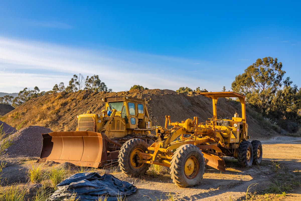 Yellow bulldozer and grader on a dirt construction site under blue sky.